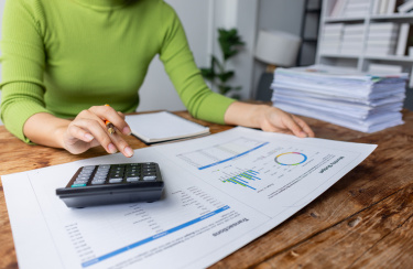 Frau sitzt am Schreibtisch und tippt auf Taschenrechner 