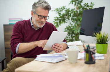 Mann sitzt im Büro am Schreibtisch und hat ein Tablet in der Hand