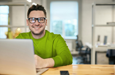 Mann arbeitet am Rechner und lächelt in die Kamera