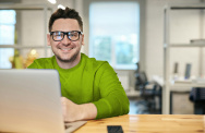 Mann arbeitet am Rechner und lächelt in die Kamera