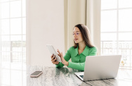 Frau sitzt am Schreibtisch und tippt auf Smartphone 