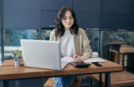 Frau arbeitet am Schreibtisch mit Laptop und Taschenrechner 