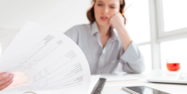 Frau blickt ratlos in unterlagen am schreibtisch