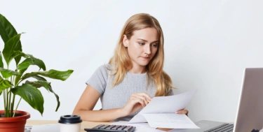 junge frau sitzt am Schreibtisch mit Papier in der Hand und prüft Unterlagen