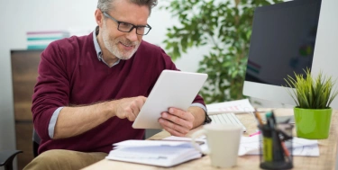 Mann sitzt im Büro am Schreibtisch und hat ein Tablet in der Hand