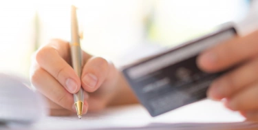  Hand mit Stift und Kreditkarte über Antragsformular