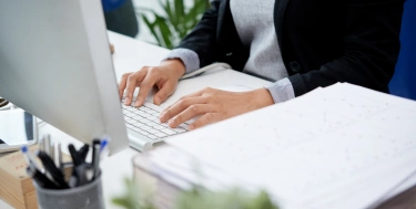 Unerkennbare Frau, die am Schreibtisch im Büro sitzt und auf Tastatur schreibt