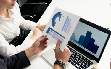 Frau und Mann vergleichen ein Blatt mit dem Laptop-Inhalt