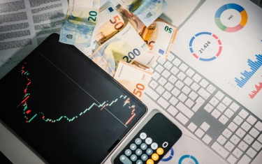 Tablet mit einer Grafik, daneben ein Taschenrechner und Geldscheine