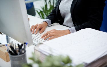 Unerkennbare Frau, die am Schreibtisch im Büro sitzt und auf Tastatur schreibt