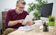 Mann sitzt im Büro am Schreibtisch und hat ein Tablet in der Hand