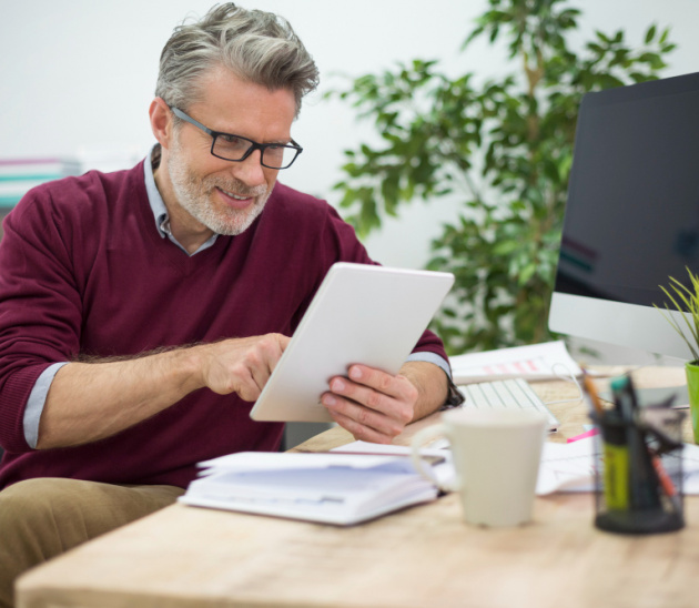 Mann sitzt im Büro am Schreibtisch und hat ein Tablet in der Hand